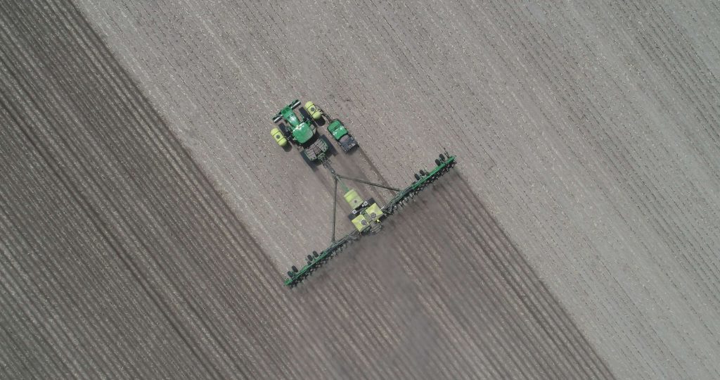 Aerial view of tractor planting rows of crops in early spring